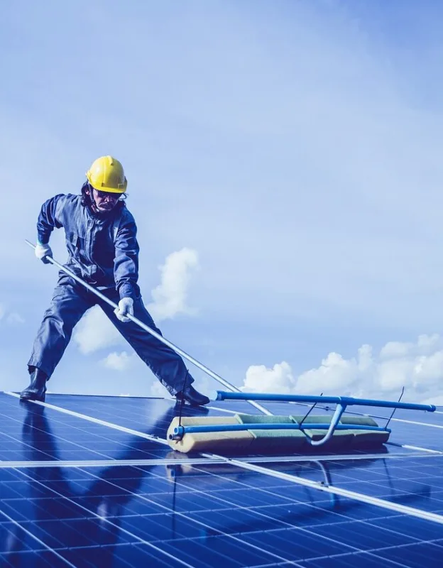 Worker cleaning solar panels with a brush on a rooftop