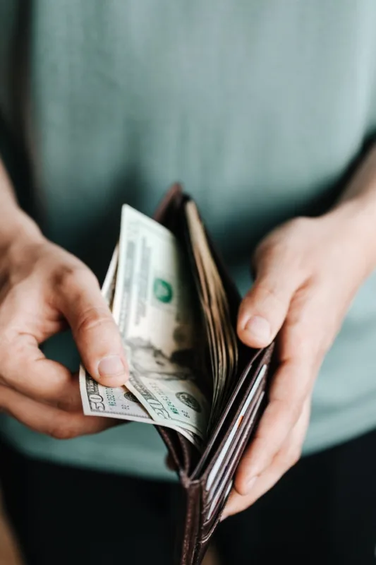 Person holding a wallet with cash, representing saving money and budgeting.