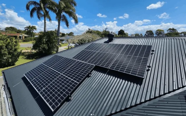 Solar panels installed on a corrugated metal roof with palm trees in the background.