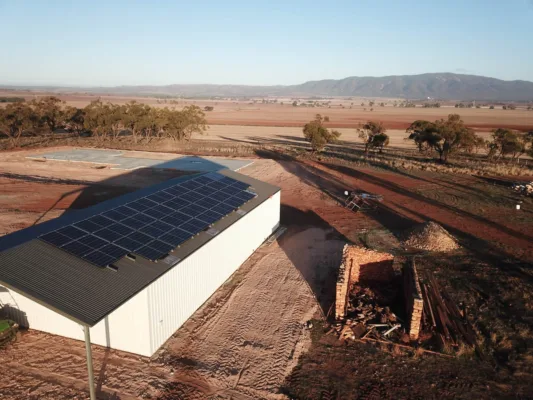 Rural building with solar panels, mountains in background. Sustainable energy.